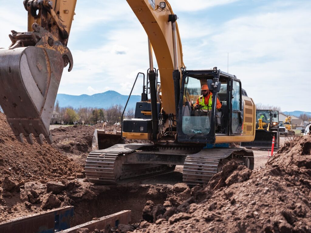 A CAT excavator wearing high-visibility clothing digging a trench at a jobsite. A heavy equipment operator controls an excavator.