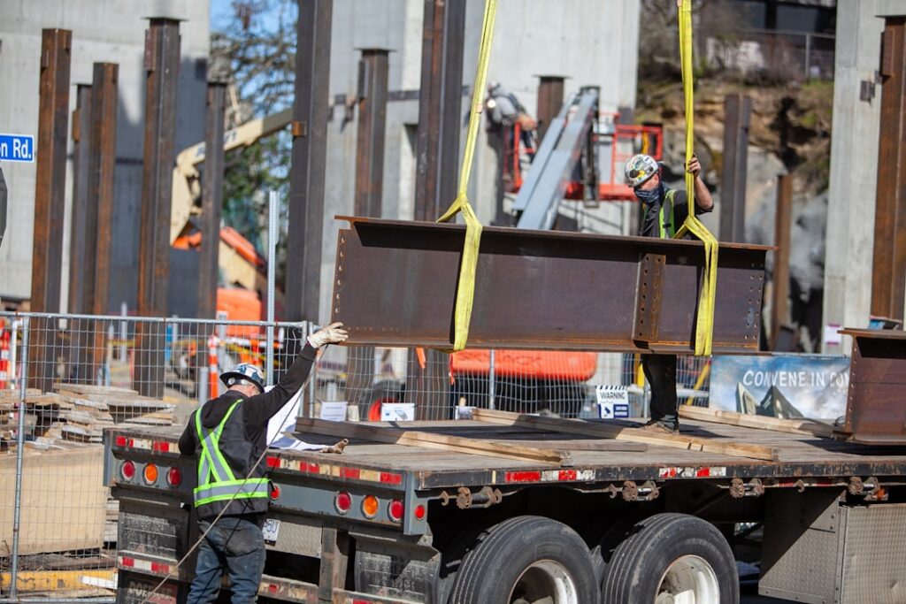 Crane lifting steel beam guided by worker